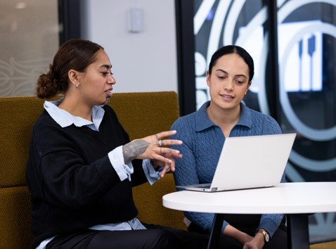 2 women sitting in front of a laptop